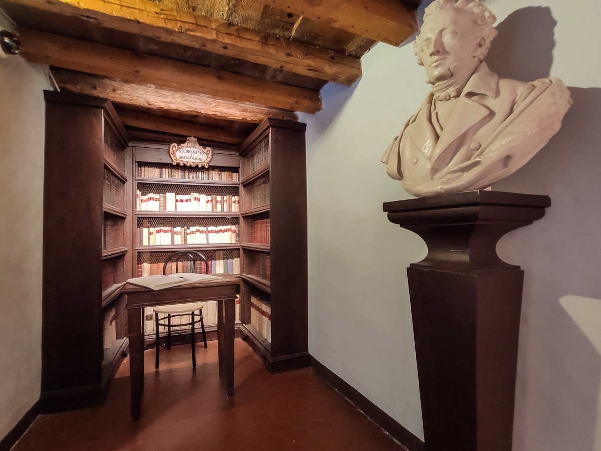 interno della biblioteca di Casa Leopardi a Recanati, scaffali lignei di libri antichi e busto del poeta