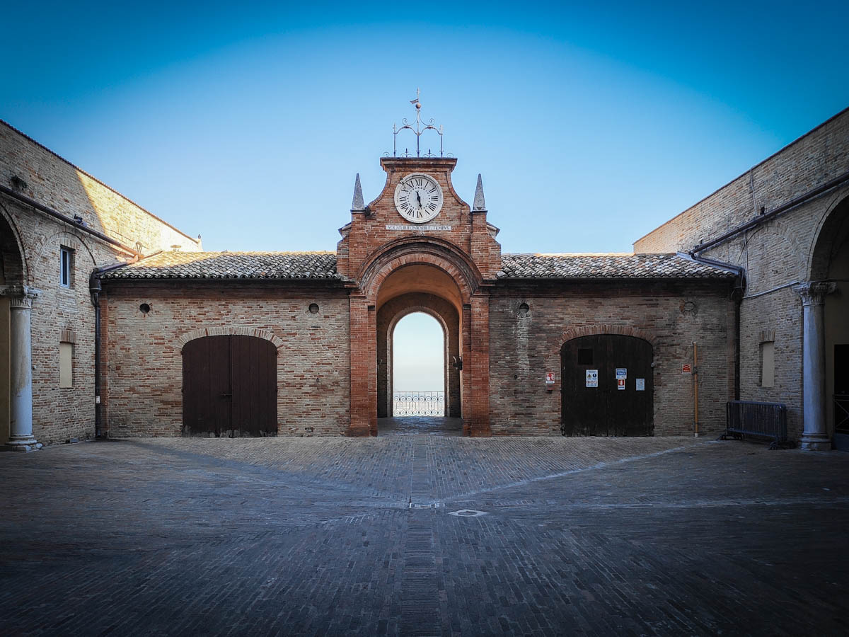 cortile di Palazzo Venieri a Recanati con l'arco e l'orologio che inquadrano il panorama verso il mare