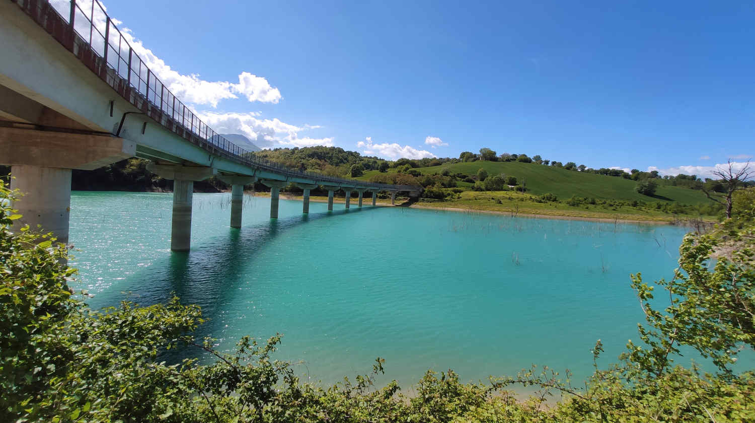 il viadotto che attraversa il Lago di Castreccioni, acqua turchese e colline verdi intorno sotto un cielo azzurro